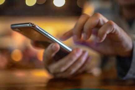 Closeup-image-of-a-man-holding-and-using-smart-phone-with-coffee-cup-on-wooden-table-in-cafe_Gettyimagesboonchai-wedmakawand