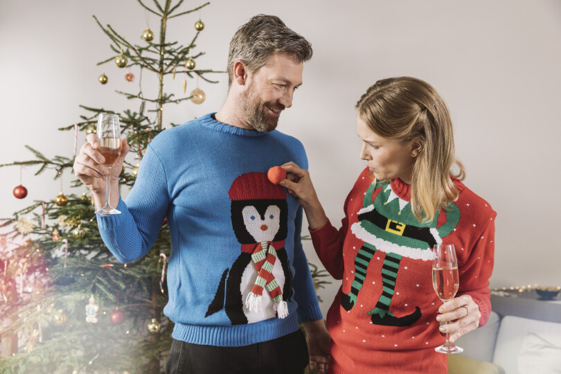 Two-people-with-ugly-Christmas-sweaters-laughing-in-front-of-tree_GettyimagesWestend61