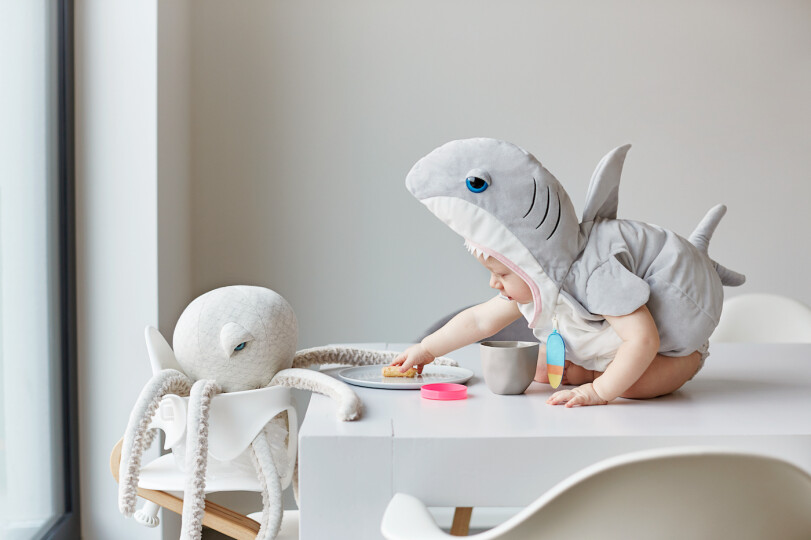 A-toddler-sits-in-a-shark-costume-on-a-table-and-gives-a-stuffed-animal-a-flip_Gettyimages2K-Studio