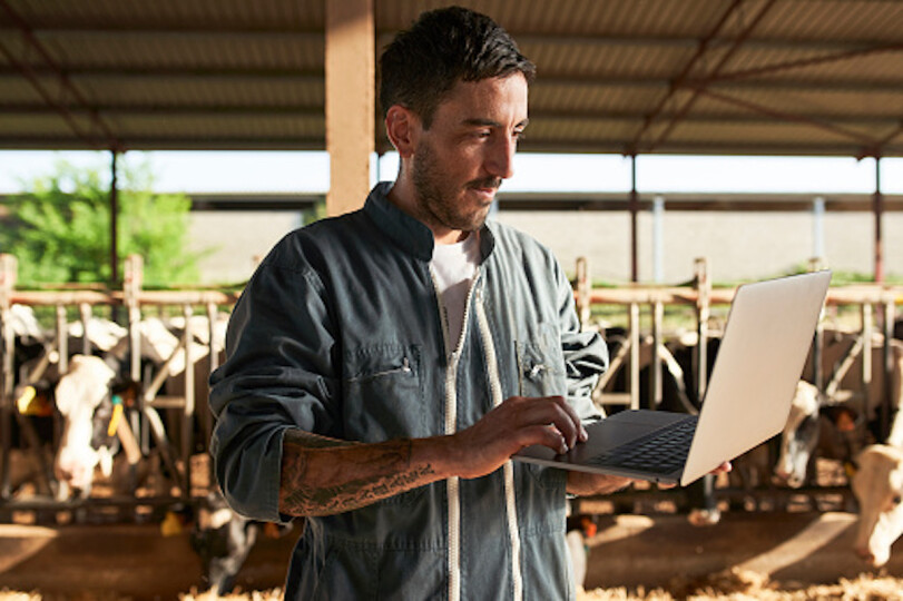 Farmer-using-laptop-while-standing-near-livestock-at-farm_GettyimagesWestend61