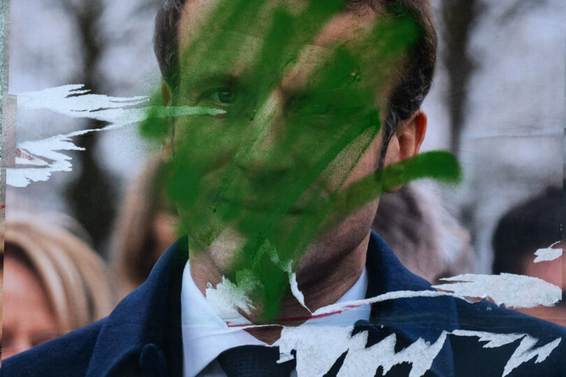 This picture taken on April 17, 2022 in Paris shows a campaign poster of France's President and La Republique en Marche (LREM) party candidate Emmanuel Macron covered of green paint to symbolize his speech on ecology between the two rounds of the Presidential election in France. (Photo by JOEL SAGET / AFP)