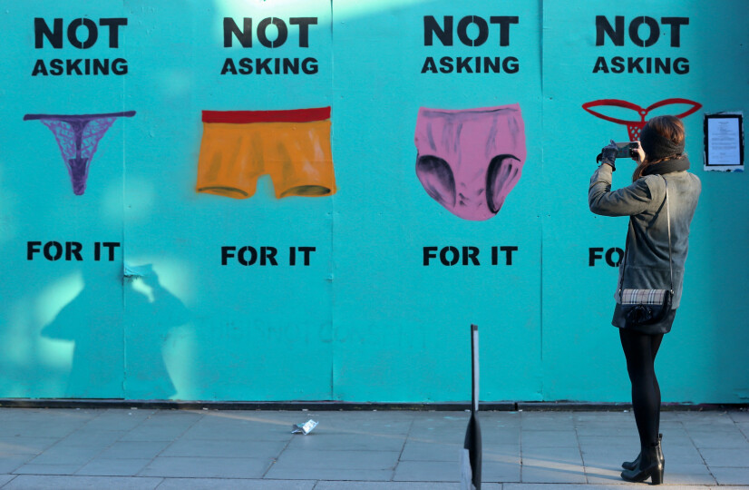 A woman stops to photograph a mural showing pictures of underwear with the slogan 'Not Asking For It' in a street in Dublin on November 17, 2018 as a protest after a defence lawyer showed a 17-year-old girl's thong or G-string in court as alleged proof of her consent in a rape case. - Protests have flared across Ireland this week triggering a viral campaign online after a defence lawyer showed a 17-year-old girl's thong or G-string in court as alleged proof of her consent in a rape case. The outrage has included a female lawmaker brandishing underwear in parliament and women posting pictures of their thongs online with the hashtag #ThisIsNotConsent. (Photo by Paul FAITH / AFP)