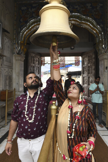 A newly married couple iadorned with flowers ring a bell as they arrive to pay their respect during Teej festival celebrated to welcome the monsoon at the Durgiana Temple in Amritsar on July 18, 2021. (Photo by NARINDER NANU / AFP)