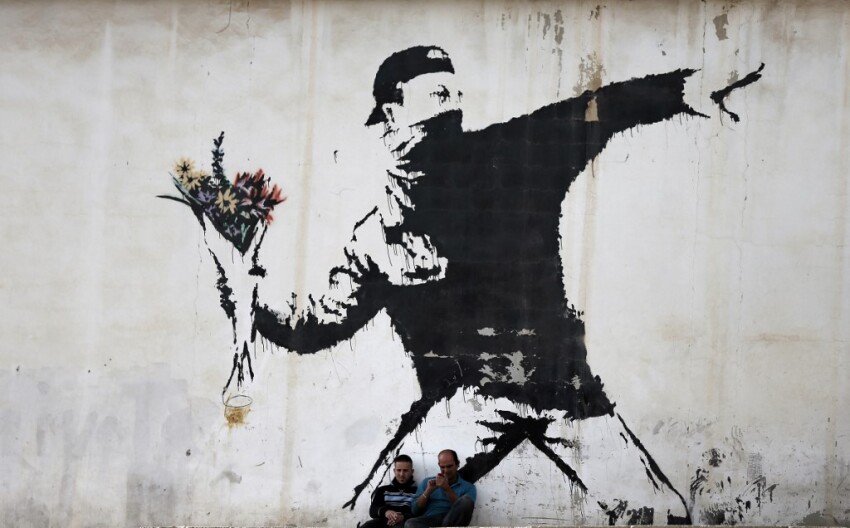 Deux hommes sont assis devant ce graffiti de Banksy à Bethléem, Décembre 2015. AFP PHOTO / THOMAS COEX