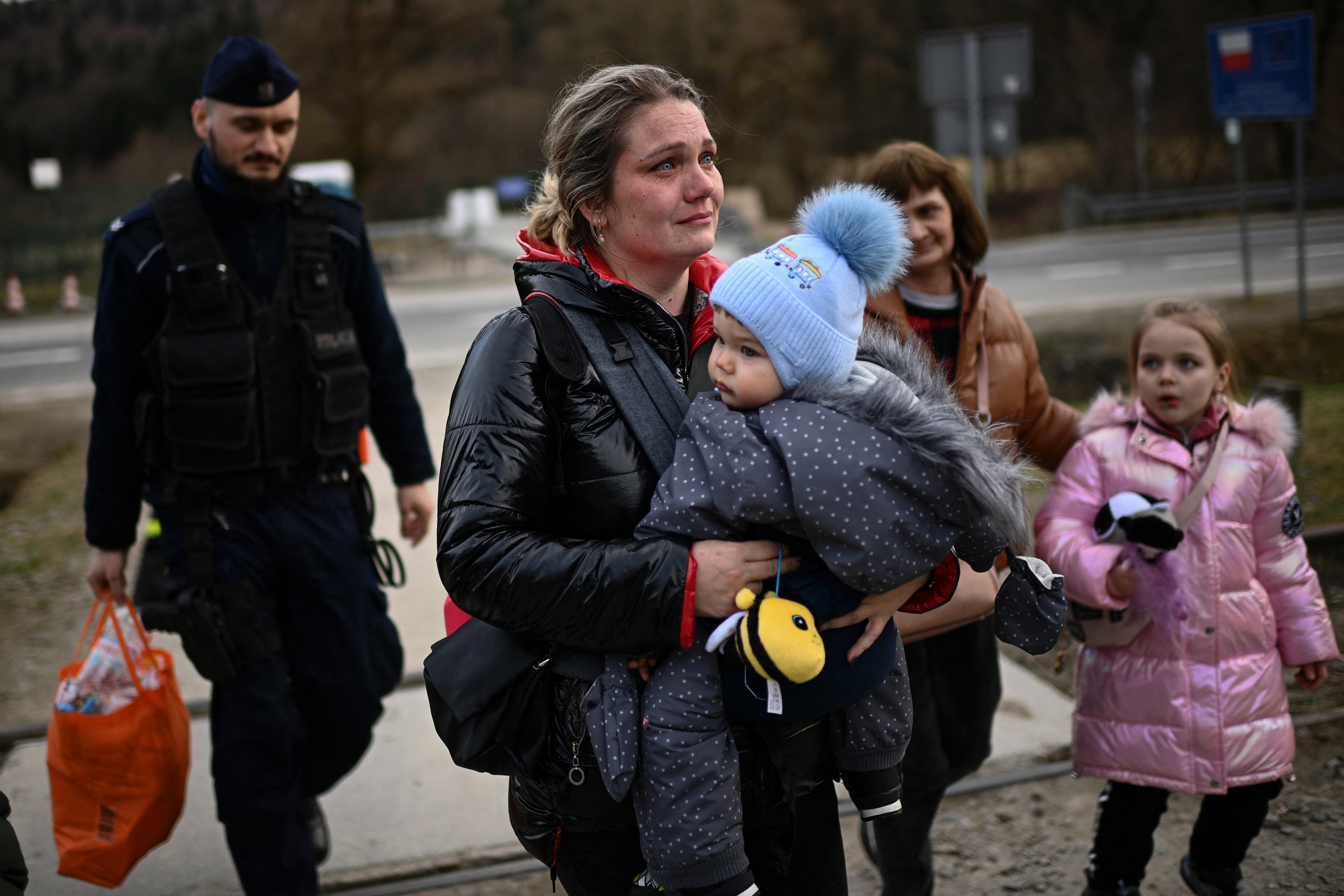 A Polish border policeman (L) carries the luggage of a Ukrainian refugee as she holds her baby after crossing the Ukrainian-Polish border into Poland along with her children at the Kroscienko border crossing, eastern Poland on April 7, 2022. (Photo by Christophe ARCHAMBAULT / AFP)